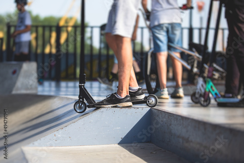 Skate park view with kids on a kick scooter doing tricks and stunts, boys in a skate park riding bmx bike and skate, playing and enjoying summer on new ramp, teenagers skateboarders and bmx riders photo