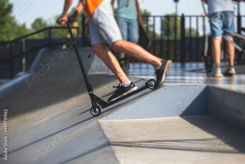 Skate park view with kids on a kick scooter doing tricks and stunts, boys in a skate park riding bmx bike and skate, playing and enjoying summer on new ramp, teenagers skateboarders and bmx riders