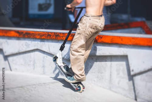 Skate park view with kids on a kick scooter doing tricks and stunts, boys in a skate park riding bmx bike and skate, playing and enjoying summer on new ramp, teenagers skateboarders and bmx riders photo