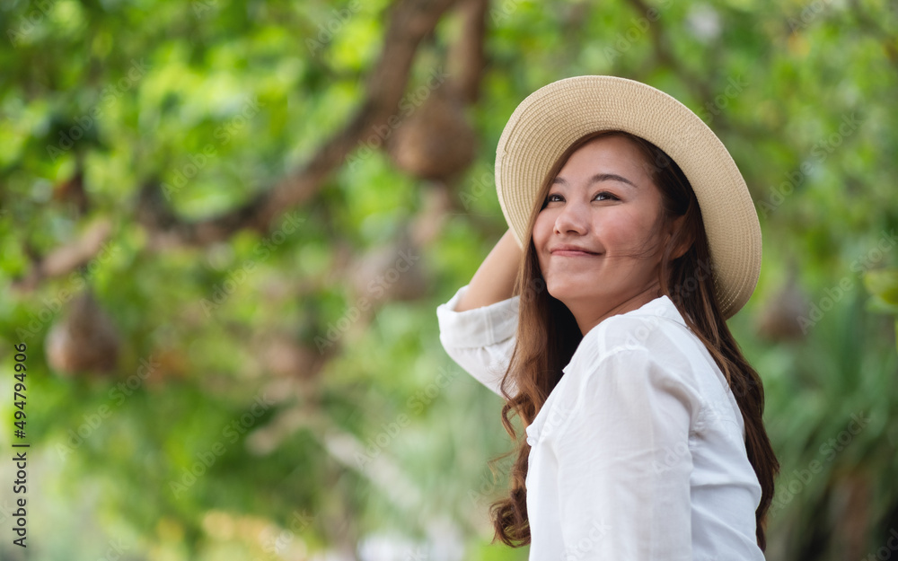 Portrait image of a beautiful young asian woman in white shirt with hat relaxing in the park