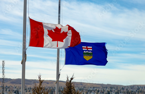 A Canadian flag and a province of Alberta Flag waving with the wind half-mast or half-staff refers to a flag flying below the summit a symbol of respect, mourning, distress, or in some cases, a salute