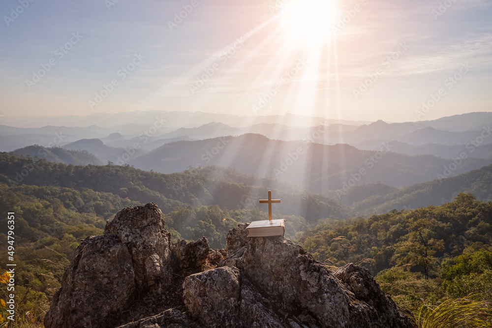 crucifix symbol and bible on top mountain with bright sunbeam on the colorful sky background
