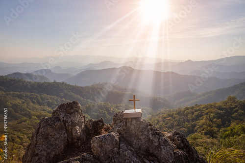 crucifix symbol and bible on top mountain with bright sunbeam on the colorful sky background