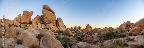 Joshua Tree National Park at sunset with large rock boulders in view and sun dipping below the horizon in the background.  photo