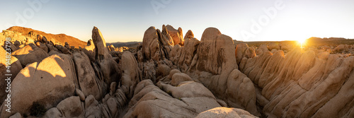 Joshua Tree National Park at sunset with large rock boulders in view and sun dipping below the horizon in the background. 