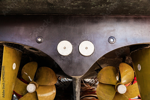 The back of a large motor yacht, standing on wooden blocks in a dry dock. Two propellers and zinc protective inserts. photo