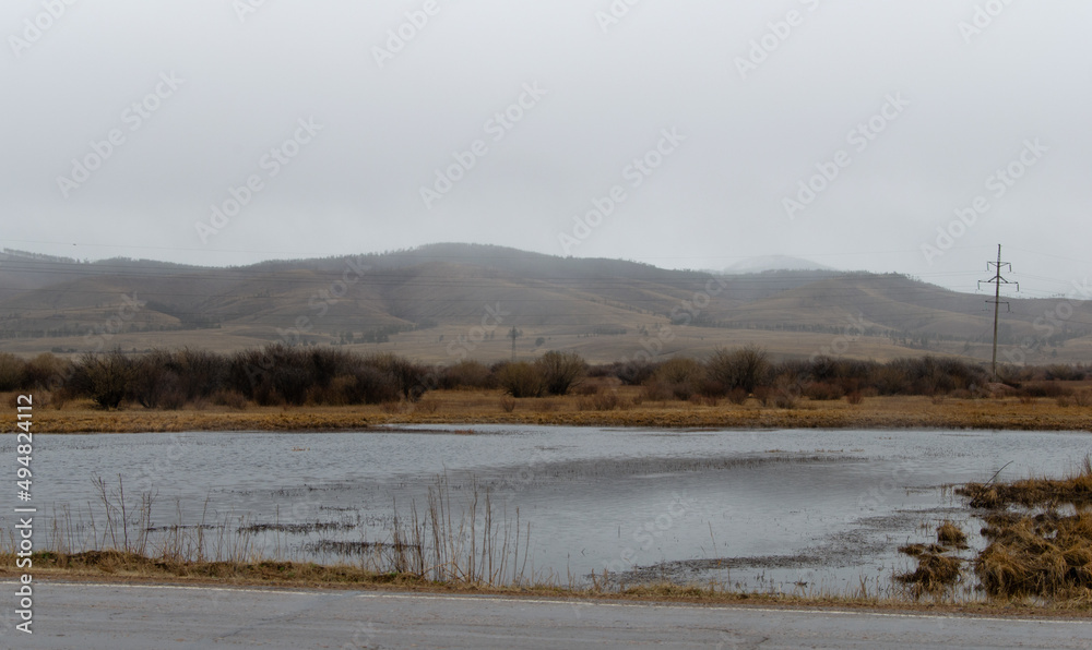 View of the river in cloudy rainy weather. Hills in the fog.