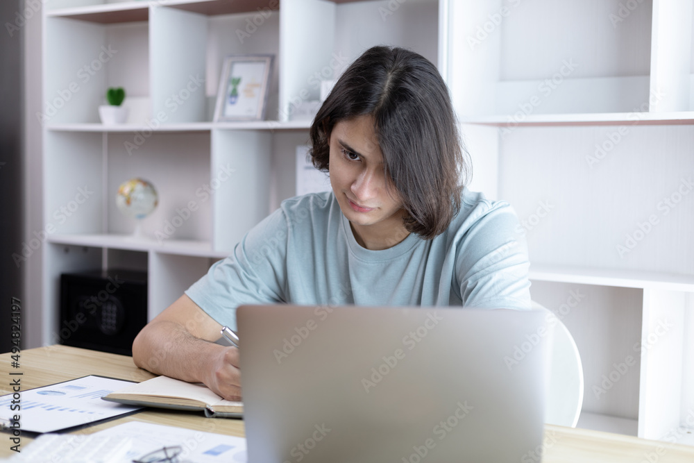 Asian man taking notes in notebook while studying online in laptop at home, Video chat, Online communication , Stay home, New normal, Distance learning.., Social distancing, Learn online... Asian man taking notes in notebook while studying online in laptop at home, Video chat, Online communication , Stay home, New normal, Distance learning.., Social distancing, Learn online...