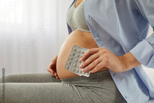 Future mother takes vitamin and mineral pills to ensure she gets enough nutrients for her baby in her womb. Pregnant woman with bare belly holding blister packs, close up. Pregnancy and health concept