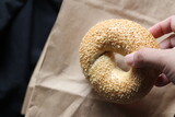 A man's hand is holding a bagel on a brown paper bag.