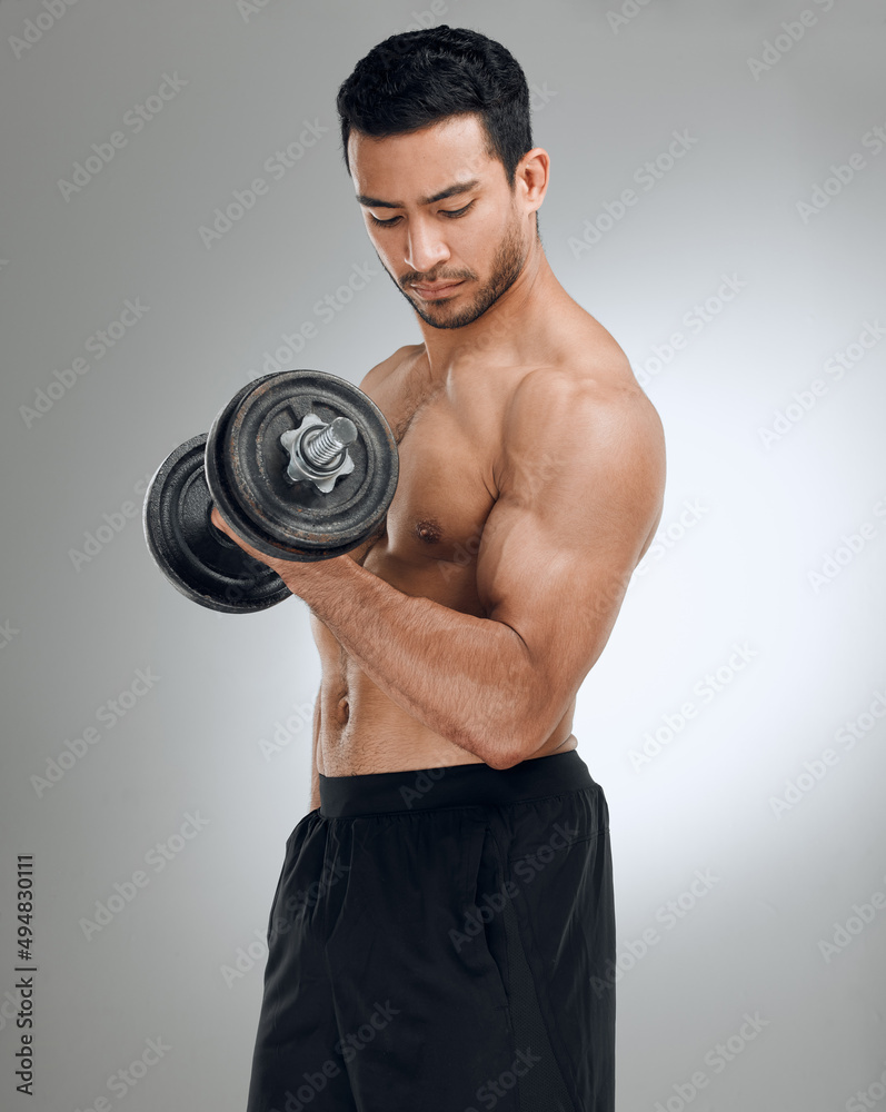 If you want to look good, you have to lift heavy. Shot of a man working out with weights while standing against a grey background. If you want to look good, you have to lift heavy. Shot of a man working out with weights while standing against a grey background.