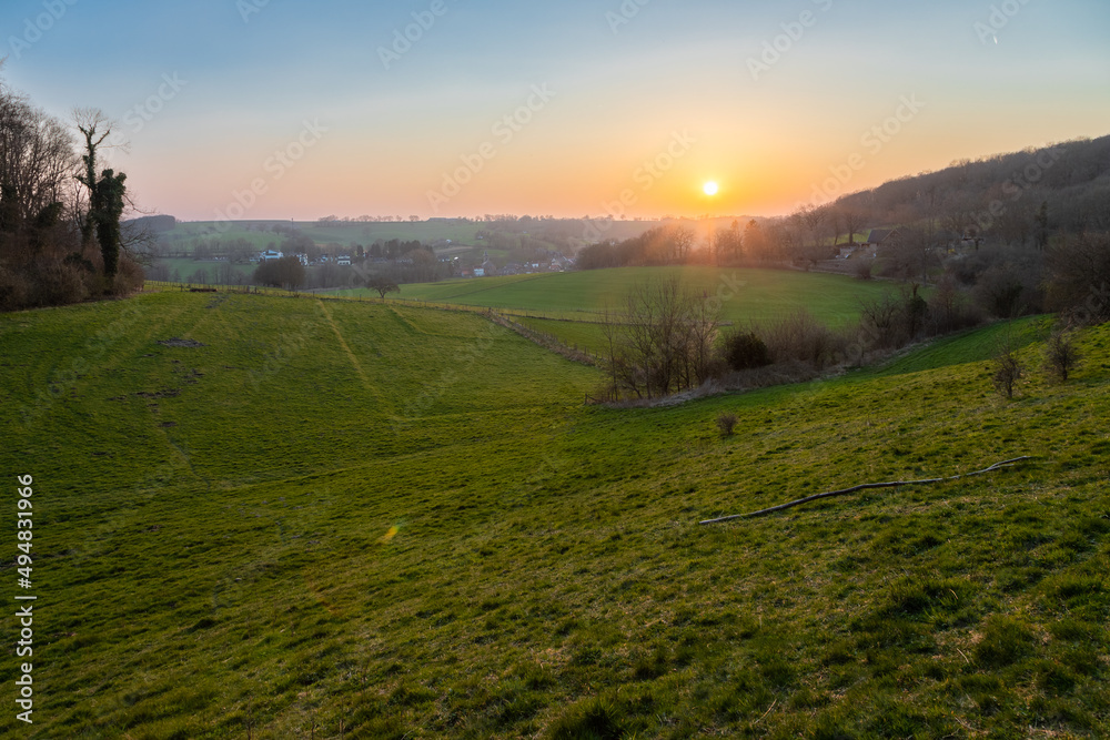 A sunset during spring over het rolling hill landscape in the south of the Netherlands with a view on the small village Slenaken, the meadows and in the background the sun going down
