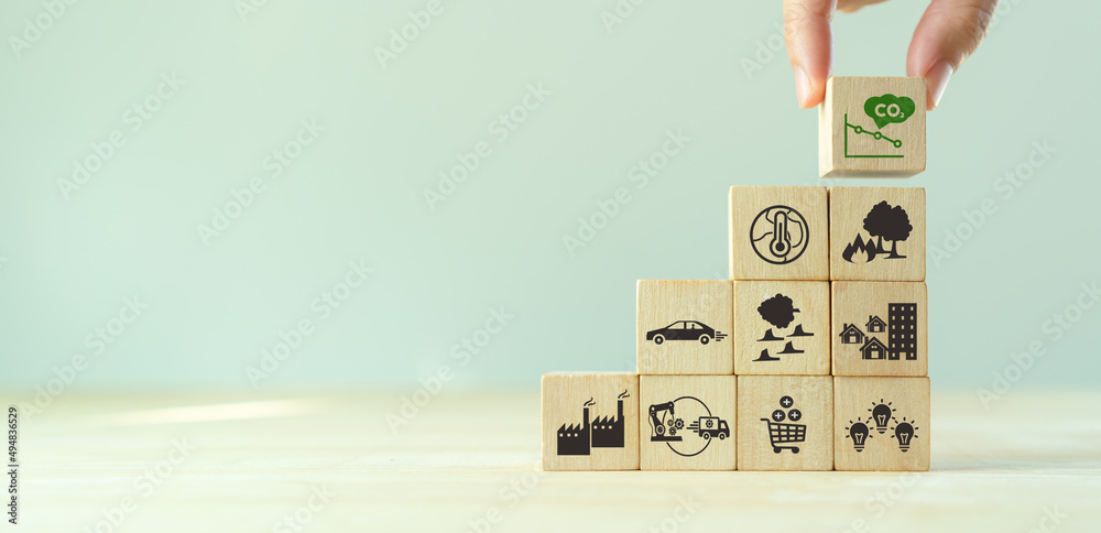 Low carbon emission and net zero concept. Climate changing problems solving goals. Stacking wooden cubes with decarbonization icon on pollution causes icons on grey background,copy space. LCA. Low carbon emission and net zero concept. Climate changing problems solving goals. Stacking wooden cubes with decarbonization icon on pollution causes icons on grey background,copy space. LCA.