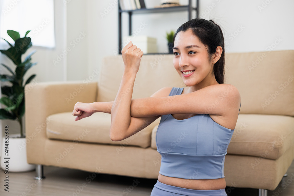 Attractive asian young fitness woman stretching arms warming up before workout at home. Beautiful smiling Female wearing sportswear exercise training yoga in living room.
