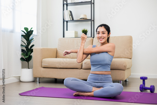 Attractive asian young fitness woman stretching arms warming up before workout at home. Beautiful smiling Female wearing sportswear exercise training yoga in living room.