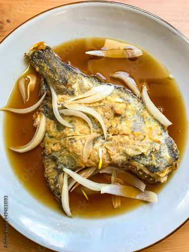 deep-fried flounder with onions and vegetables in Asian sauce on a plate.