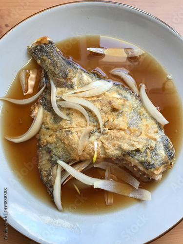 deep-fried flounder with onions and vegetables in Asian sauce on a plate.