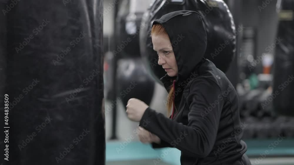 red-haired woman hits a punching bag in the gym without gloves, outburst of emotions, aggression red-haired woman hits a punching bag in the gym without gloves, outburst of emotions, aggression