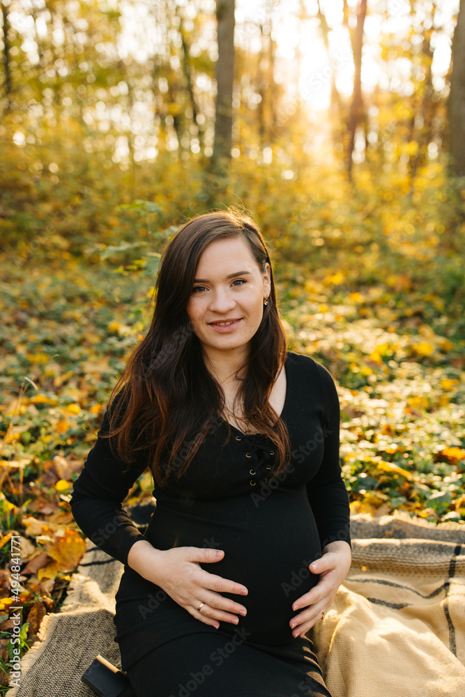 Beautiful pregnant woman in a black dress in the autumn park. Golden autumn. Fallen leaves. Awaiting the birth of a child. Beautiful pregnant woman in a black dress in the autumn park. Golden autumn. Fallen leaves. Awaiting the birth of a child.
