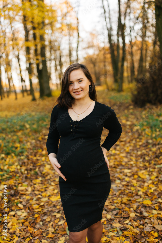Beautiful pregnant woman in a black dress in the autumn park. Golden autumn. Fallen leaves. Awaiting the birth of a child. Beautiful pregnant woman in a black dress in the autumn park. Golden autumn. Fallen leaves. Awaiting the birth of a child.