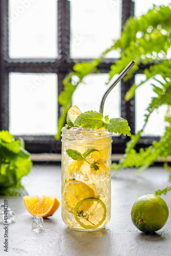 Iced tea in a beautiful glass with lime slices and red syrup, stands on a table in the backlight, a window on the back surface and flowers, a transparent tasty drink with vitamins