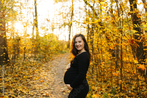 Beautiful pregnant woman in a black dress in the autumn park. Golden autumn. Fallen leaves. Awaiting the birth of a child. © Anhelina Tyshkovets