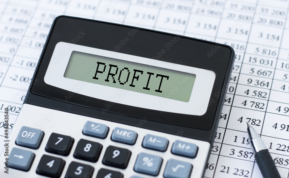 PROFIT inscription on the calculator screen on the background of reports on the table PROFIT inscription on the calculator screen on the background of reports on the table