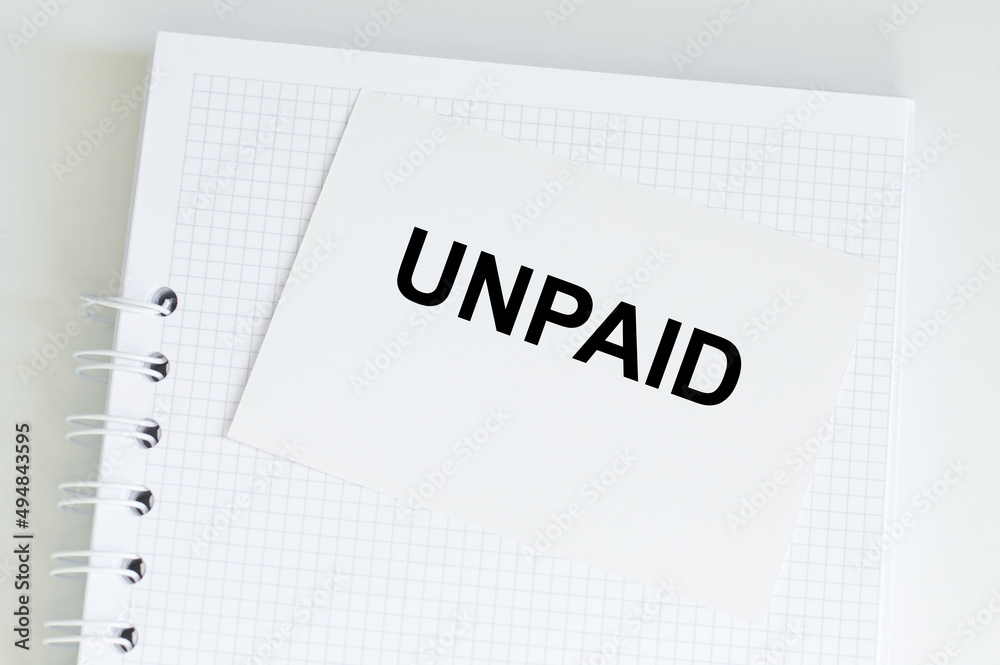 UNPAID inscription on a white card on the background of a blank notebook on the table UNPAID inscription on a white card on the background of a blank notebook on the table