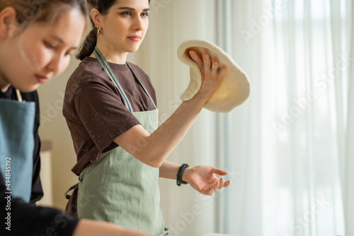 Two young female chefs cooking pizza in the kitchen, one twists the rolled dough in her hand.