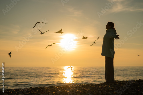 Caucasian woman spread her arms like wings on the seashore at sunset. 