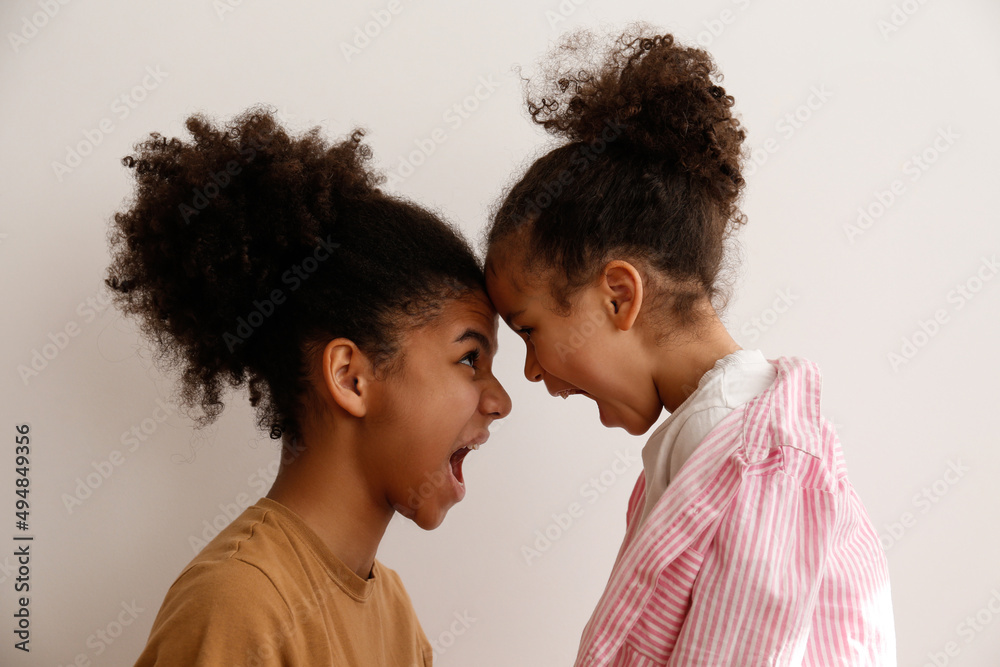 Younger and older sister in a state of emotional stress displeased with each other. Two black girls of different age arguing. Black female siblings having a fight. Background, copy space, close up. - obrazy, fototapety, plakaty 