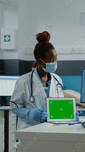 Patient and medic looking at horizontal green screen on tablet and wearing face masks for protection. Woman and doctor doing checkup with chroma key and isolated mockup template. © DC Studio