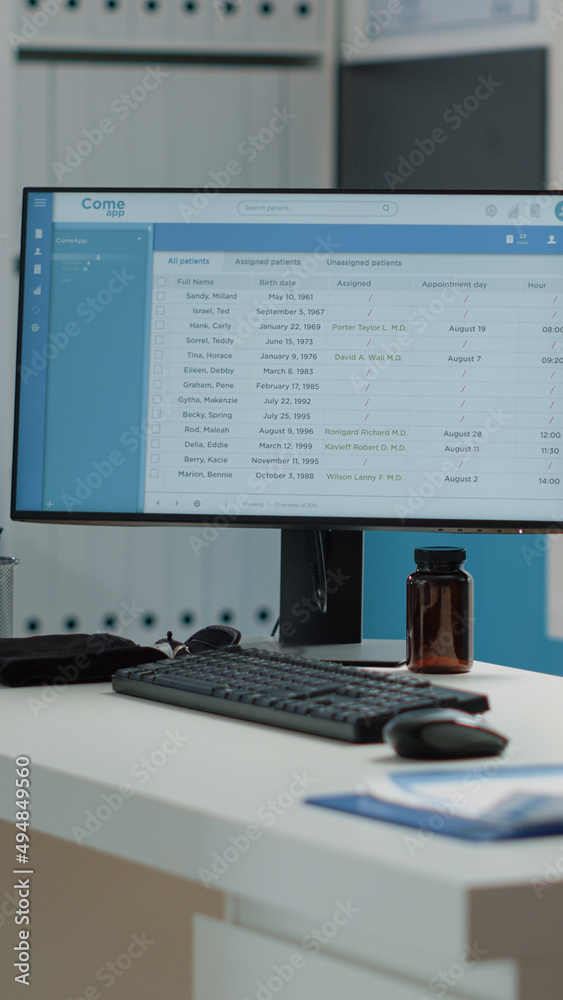 © DC Studio - Close up of computer screen with patient information on desk in empty medical cabinet. Nobody in doctors office with healthcare equipment and instruments for consultation and examination
