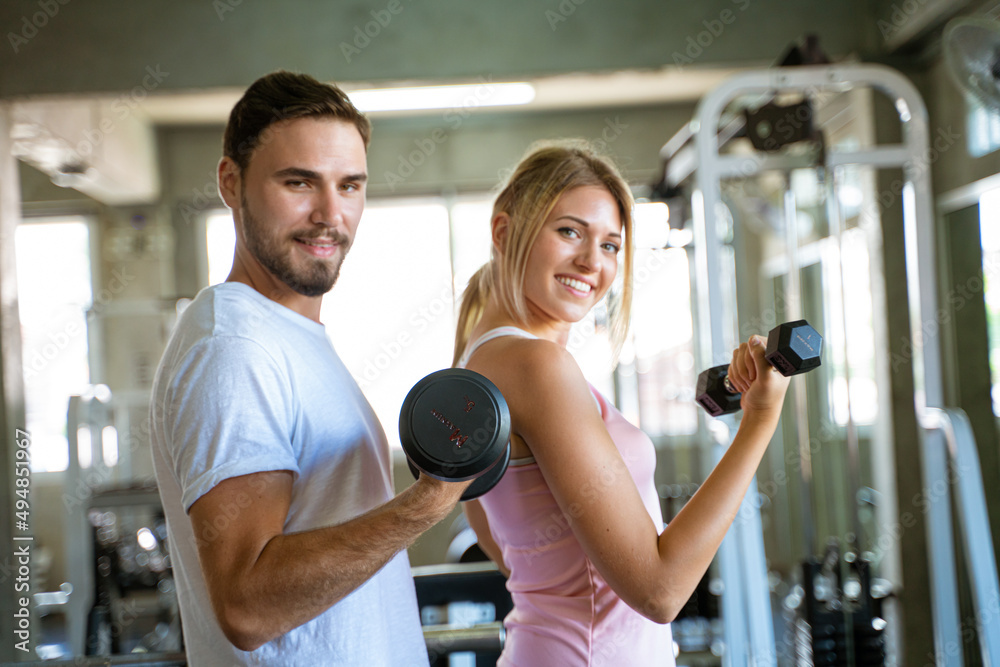 Fototapeta premium Couple lifting dumbbell in fitness gym man couching women in sport gym
