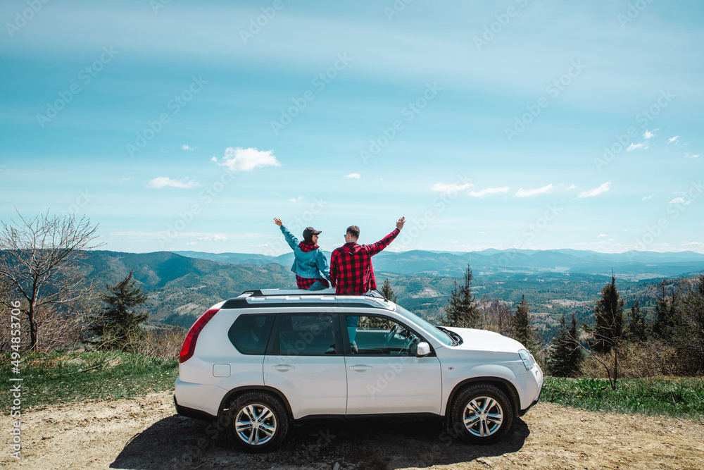 young woman sitting on the top of the suv car at mountain peak enjoying the landscape view