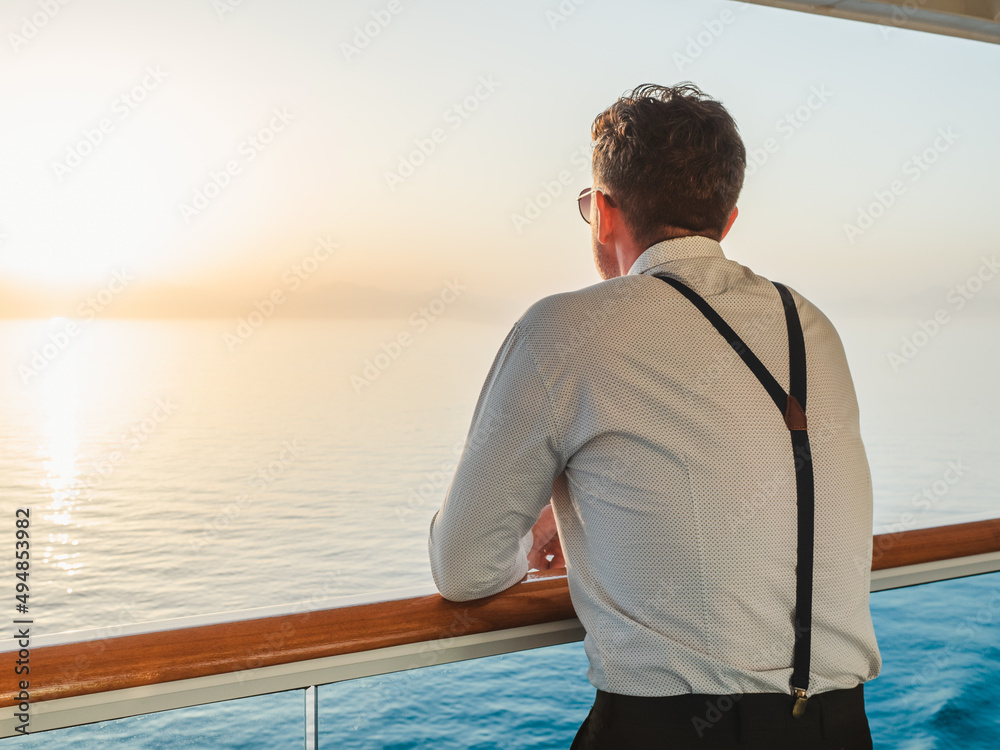 Fashionable man standing on the empty deck of a cruise liner against the backdrop of the setting sun. Closeup, outdoor. Vacation and travel concept Fashionable man standing on the empty deck of a cruise liner against the backdrop of the setting sun. Closeup, outdoor. Vacation and travel concept
