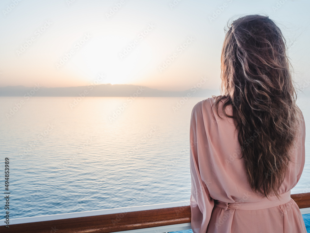Beautiful woman standing on the empty deck of a cruise liner against the backdrop of the setting sun. Closeup, outdoor. Vacation and travel concept