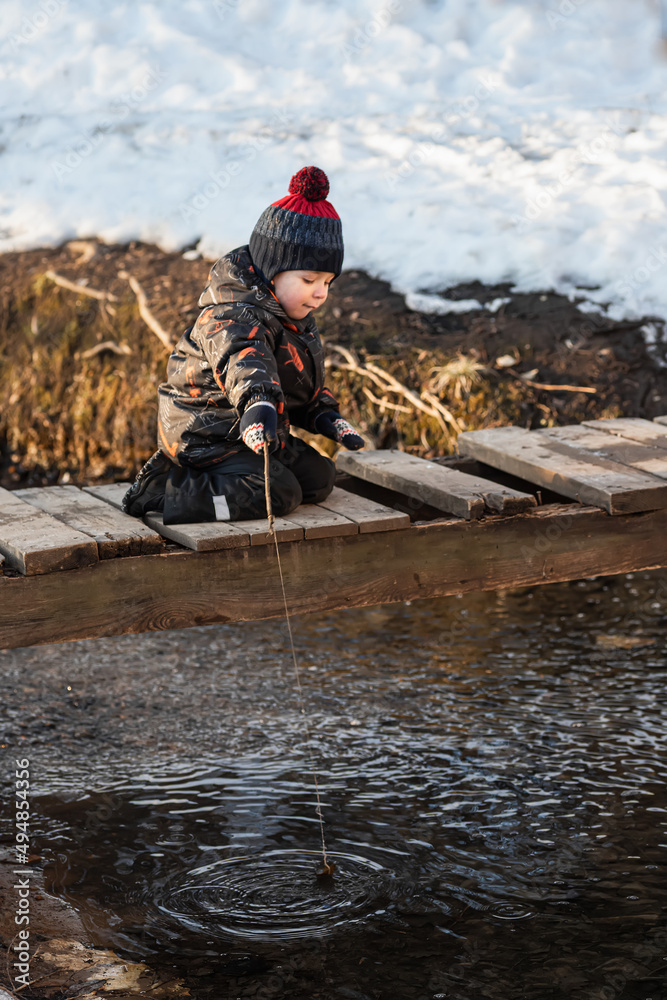 A little boy in the park in early spring. A child is playing with a homemade fishing rod made of a stick. A carefree childhood. A little boy in the park in early spring. A child is playing with a homemade fishing rod made of a stick. A carefree childhood.
