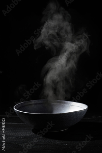Empty soup bowl with steam in a dark kitchen. Black background. Surreal dark food photography concept. 