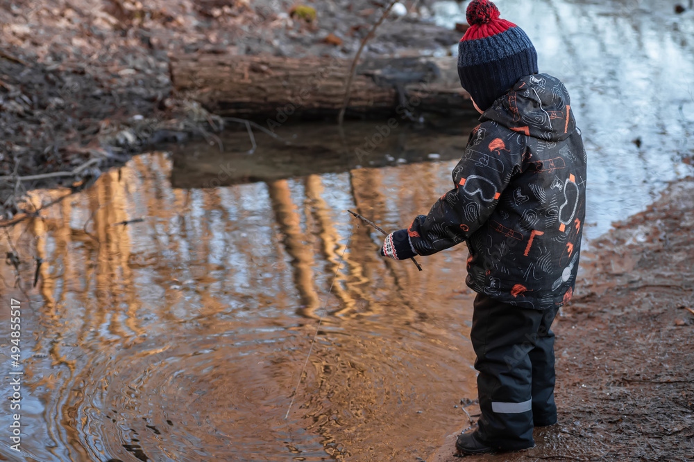 A little boy in the park in early spring. A child is playing with a homemade fishing rod made of a stick. A carefree childhood. A little boy in the park in early spring. A child is playing with a homemade fishing rod made of a stick. A carefree childhood.