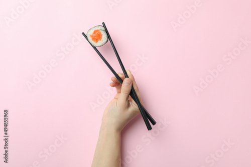 Female hand hold chopsticks with maki on pink background