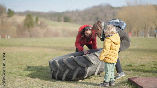 Grandchild observe mother and grandmother lift old tractor tire in park
