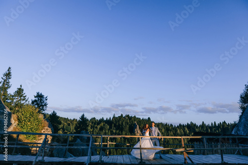After the wedding, a cheerful couple are dancing on the bridge against the backdrop of beautiful mountains and green forest.