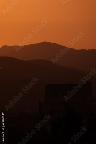 Silhouette of a castle on top of a hill with the silhouette of mountains at sunset.