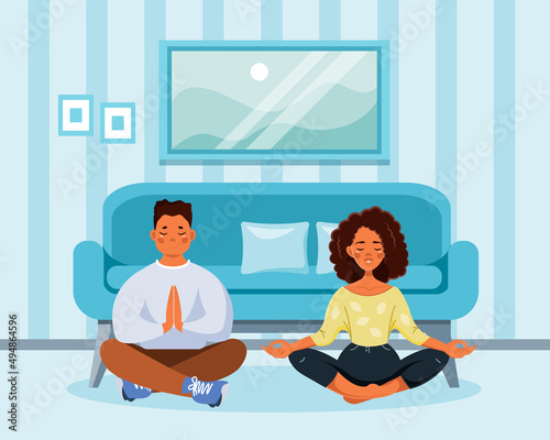 An African-American couple meditates in the lotus position in the living room