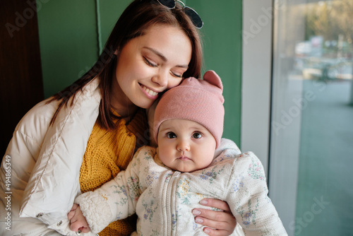 Mother holding baby smiling to camera. Real life authentic casual mom looking to camera holding