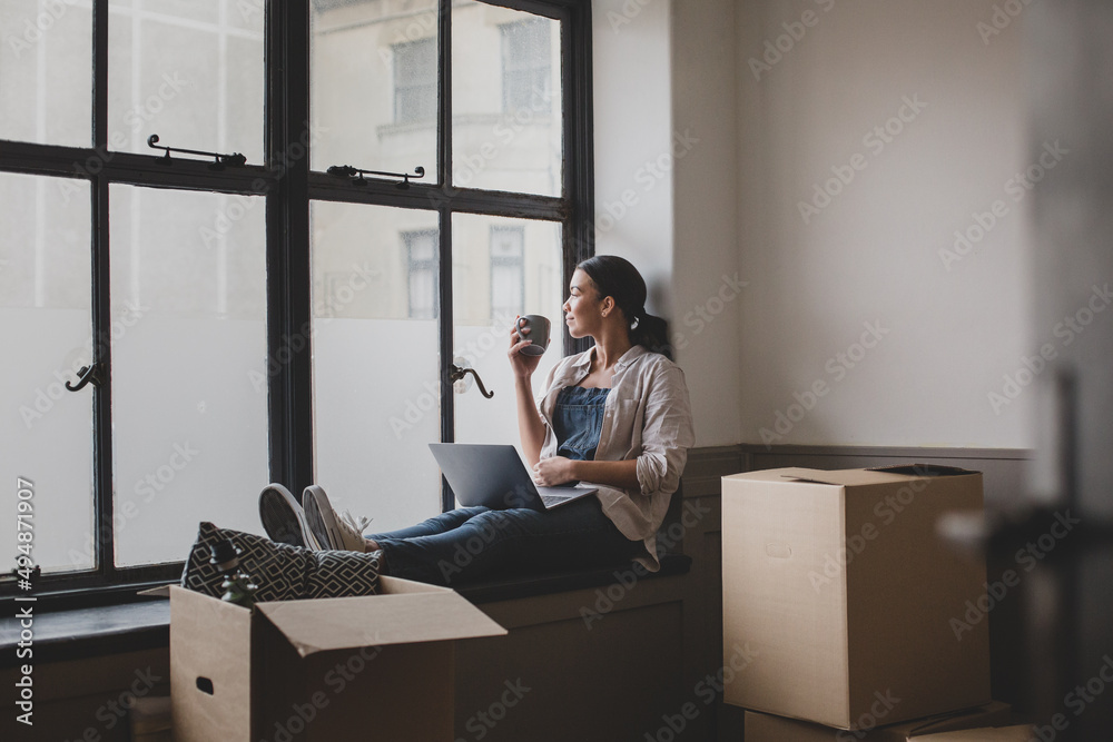 Mid adult female using laptop in new home planning and surrounded by boxes