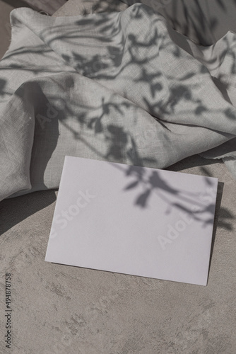 Monochrome still life with paper card mock up, linen cloth and leaf shadows on surface.