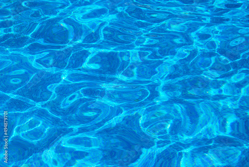 Clear water surface, ripple water in tiled swimming pool with sun reflection