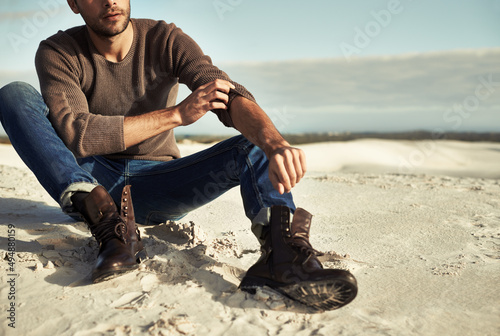 Seaside moments. A man wearing jeans and boots sitting on the beach.